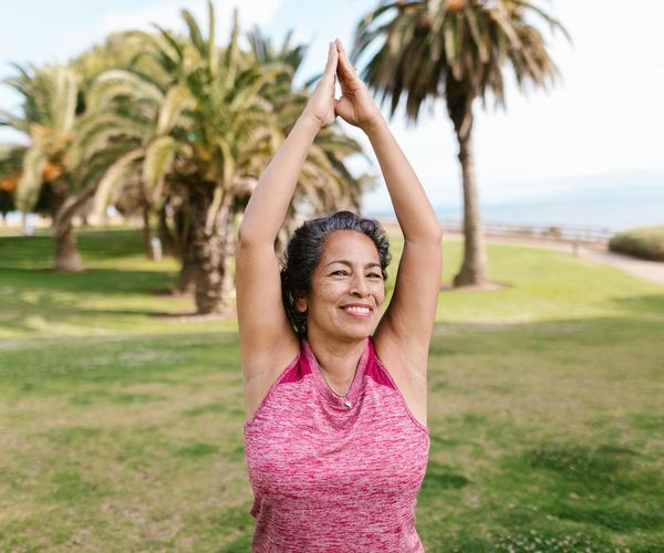 Smiling woman stretching outdoors in a green sunny park.